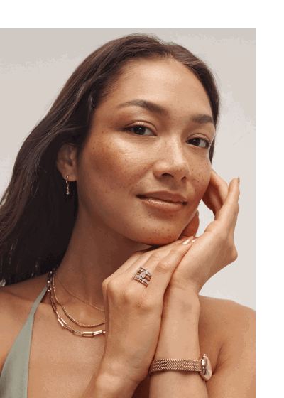 Close up of woman wearing three yellow gold chain necklaces, stacked rings and gold watch. 
