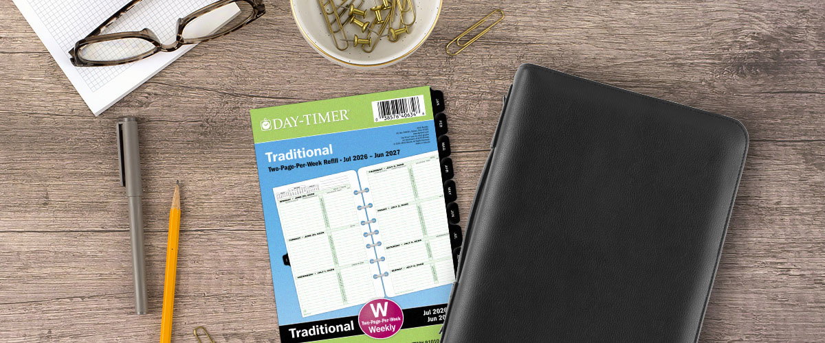 Planner refill pages and black leather planner cover on a table next to pen, pencil and paperclips 