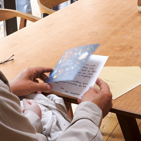 Hands opening a heartfelt Father’s Day card at a wooden table beside a cream envelope, capturing a quiet and personal family moment. Soft natural lighting and handwritten message create a warm, emotional feel.