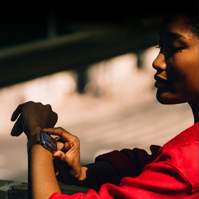 A person in a red jacket looks at a smartwatch on their wrist, with a blurred background.