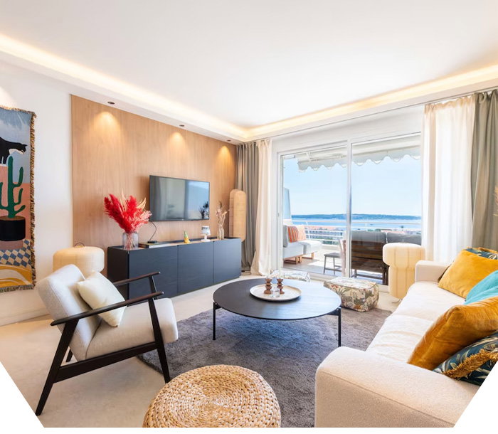 Modern living area with couches, coffee table, wall-mounted TV, and sliding doors opening to a balcony view.