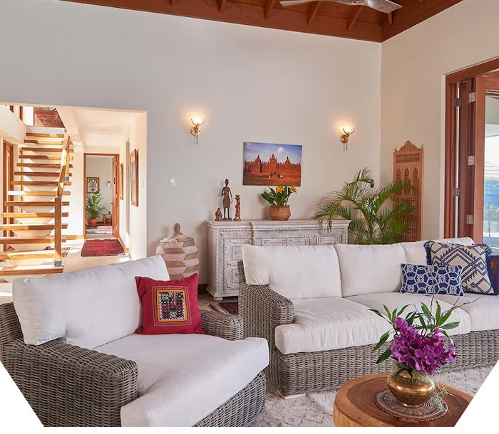 Airy living area with wicker sofa, patterned pillows, wood ceiling, console table, and glass doors.