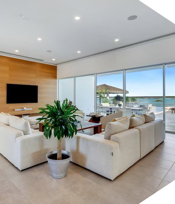 Contemporary family room with sectional, potted plant, TV wall, and ocean-view patio beyond glass doors.