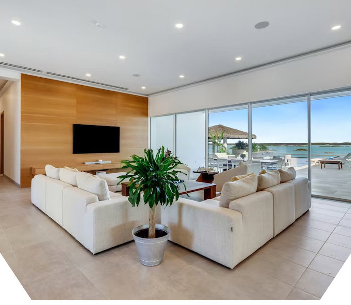 Contemporary family room with sectional, potted plant, TV wall, and ocean-view patio beyond glass doors.