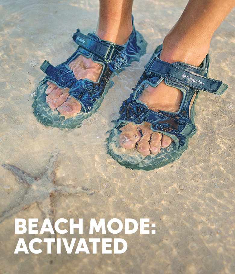 Close-up of someone's sandaled feet as they stand in the water with text: BEACH MODE: ACTIVATED