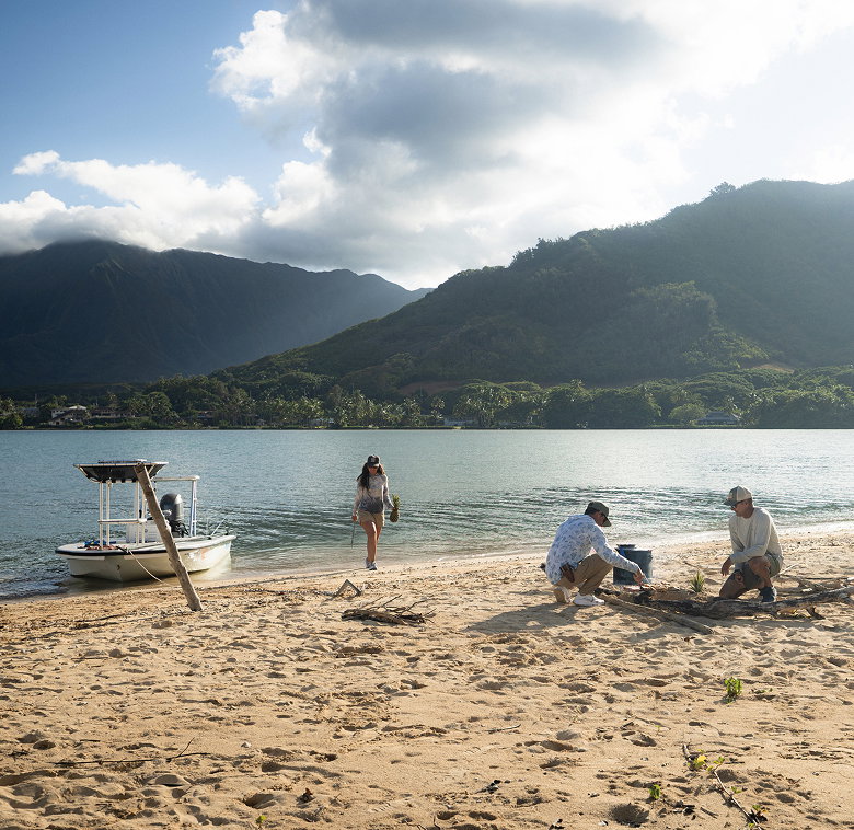 A group of people hanging out on the beach. Their boat sits at the shore.