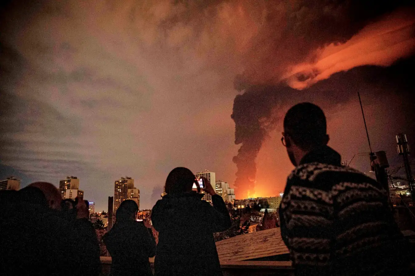People in Tehran looking towards a burning oil refinery. Image links to story