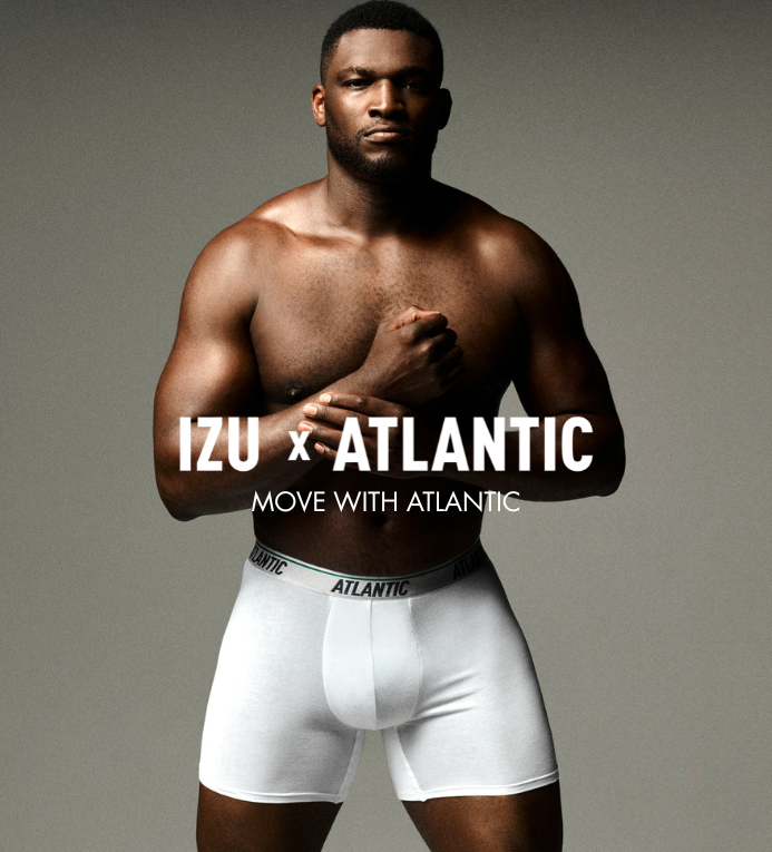 Male model wearing white Atlantic-branded boxer briefs, muscular torso with arms crossed in studio ad reading IZU x ATLANTIC