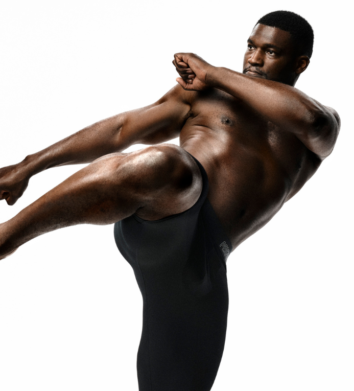 Muscular man performing a high kick wearing black compression leggings on white background, fitness and athletic action