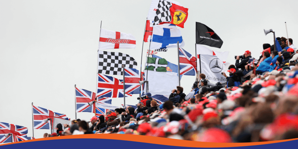 A crowd of fans at a sporting event, waving various flags, including British and team banners.