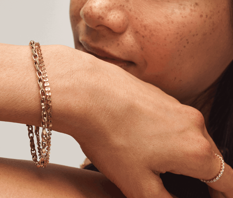 Close-up of a woman wearing two yellow gold chain bracelets and a yellow gold diamond band on her index.