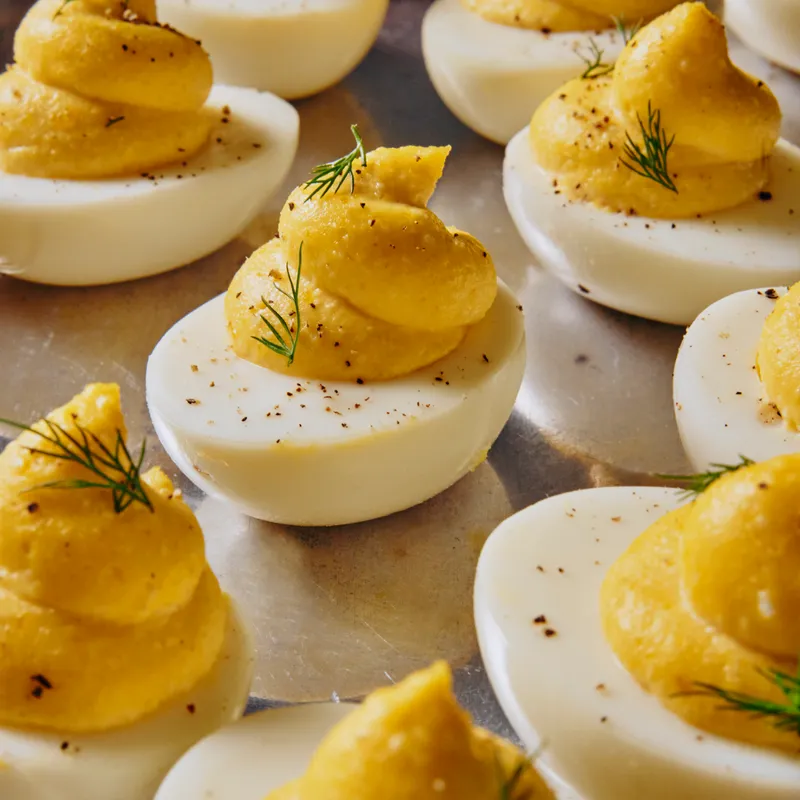 A multitude of deviled eggs, garnished generously with pepper and dill sprigs, on a reflective silver platter.