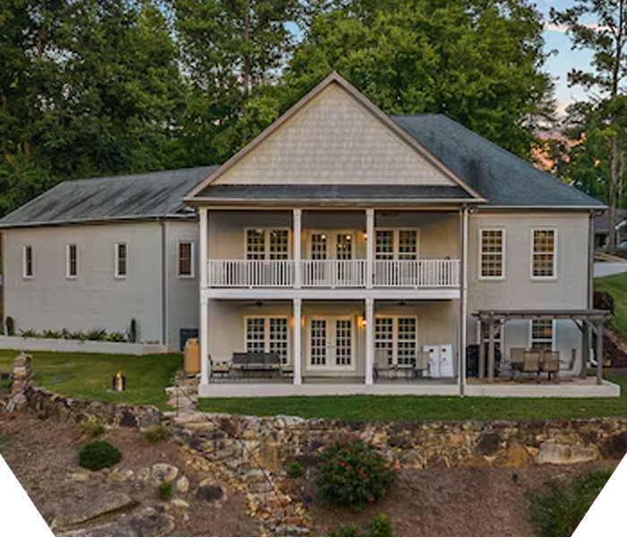 Two-story house with a covered front porch, light-colored exterior, and trees in the yard.