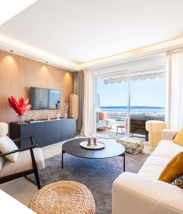 Modern living area with couches, coffee table, wall-mounted TV, and sliding doors opening to a balcony view.