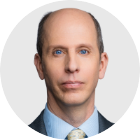Anthony Zurcher looks directly into the camera with a blue shirt, grey jacket and grey tie. His portrait image is set on a grey background