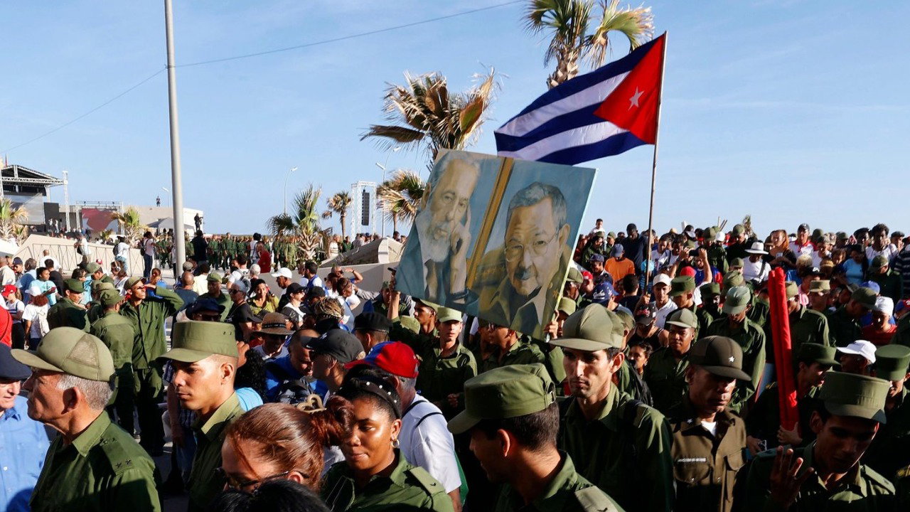 People attend an event in support of former Cuban President Raul Castro in Havana, Cuba, 22 May 2026.There is a Cuban flag, palm trees and blue skies behind the crowd.