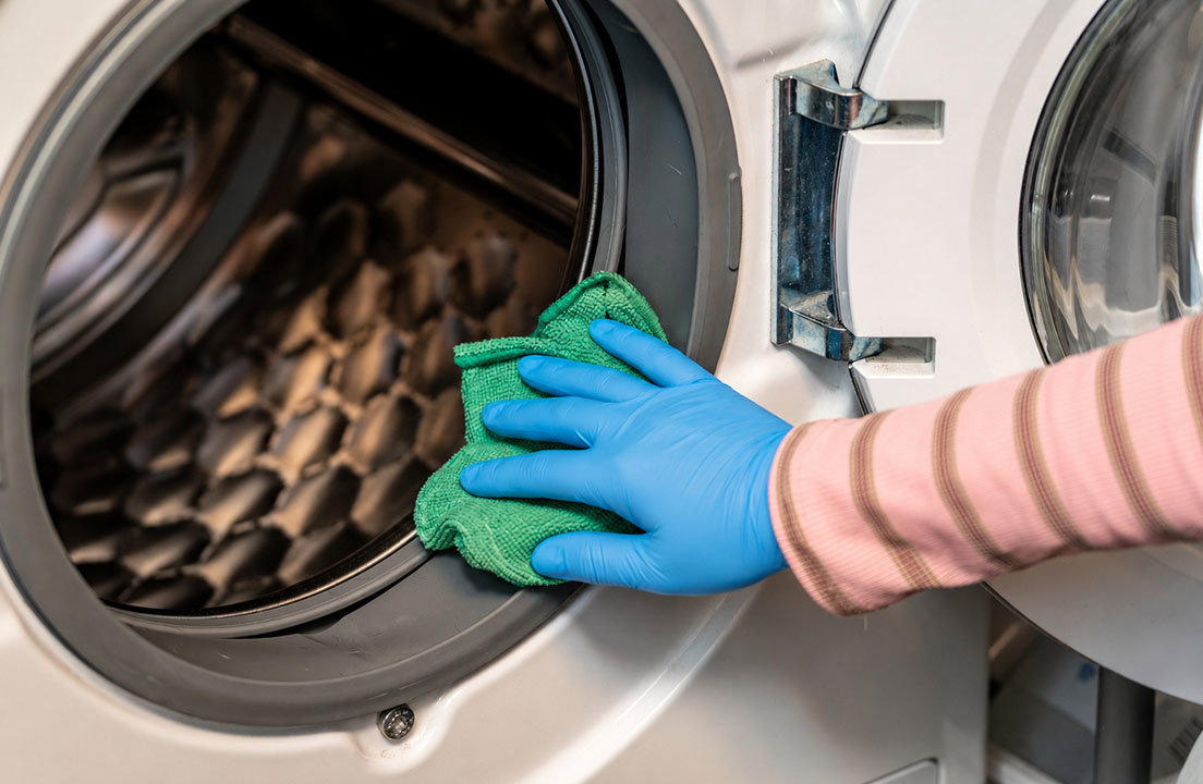 Blue gloved hand cleaning the gasket of a front load washer