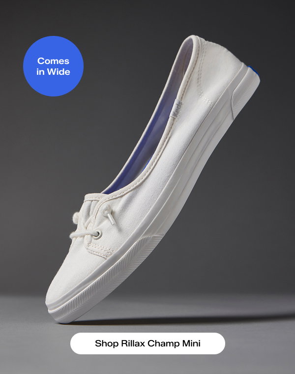 A close-up view of the Rillax Champ Mini Slip‑On in white against a dark grey background, toe on the ground and the heel in the air. A callout on the image notes that the style Comes in Wide. Shop Rillax Champ Mini.