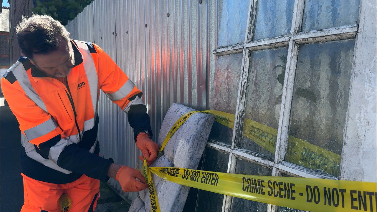 One of Luton's fly-tipping investigators, wearing orange protective clothing, ties yellow tape around dumped furniture