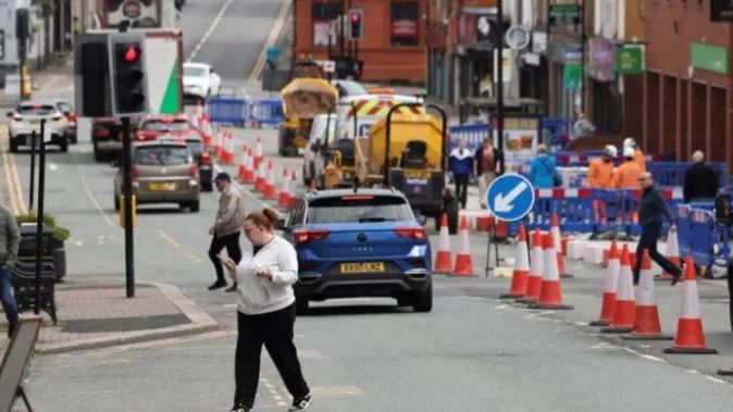 image of a street in Makerfield, with a woman crossing the oad, a blue car and roadworks