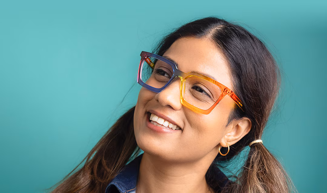 Smiling woman with pigtails, wearing The Collection Nobel multi-coloured rectangular glasses, against a teal background