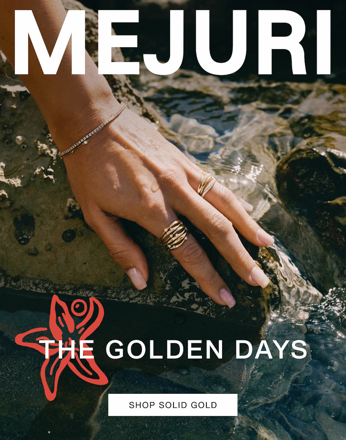 Hand resting on rocks near water wearing Mejuri gold rings and a diamond tennis bracelet — The Golden Days — Shop Solid Gold.