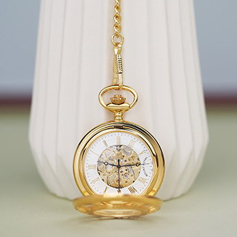 Open gold-plated pocket watch with chain hanging down a ceramic vase. - Jewellery Collection.