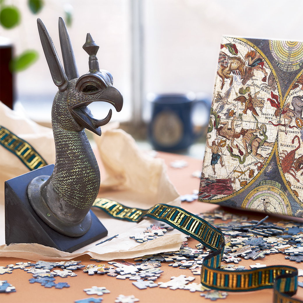 Griffin-shaped bookend beside celestial-themed jigsaw puzzles with scattered pieces on a desk with ribbon and wrapping paper. - Shop Father's Day.