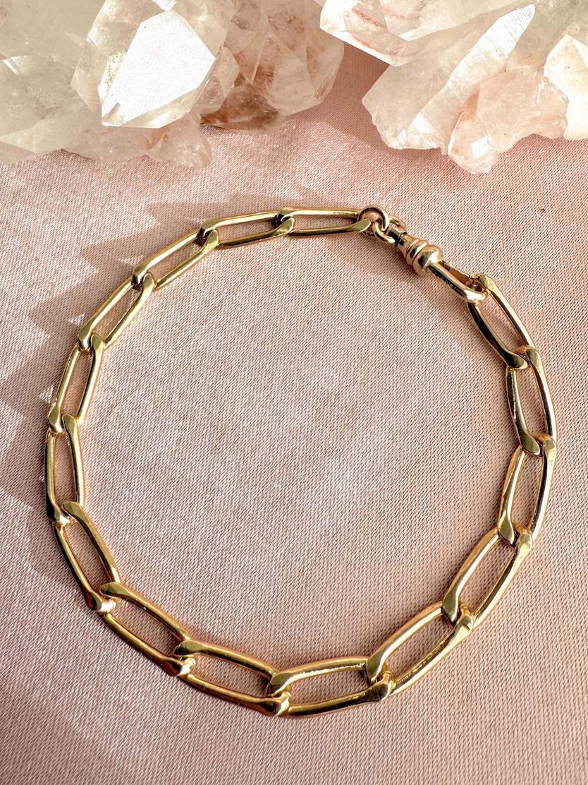 Gold-filled paperclip chain bracelet styled on a pink satin surface with quartz crystals.
