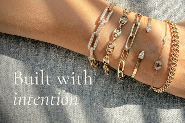 Camille Jewelry — Built with intention. Multiple gold bracelets stacked on a wrist, featuring chain links, diamond accents, and an initial charm.
