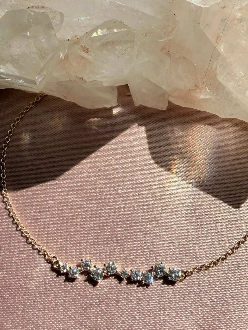 Diamond cluster bracelet with gold chain, styled on a pink satin surface with quartz crystals.