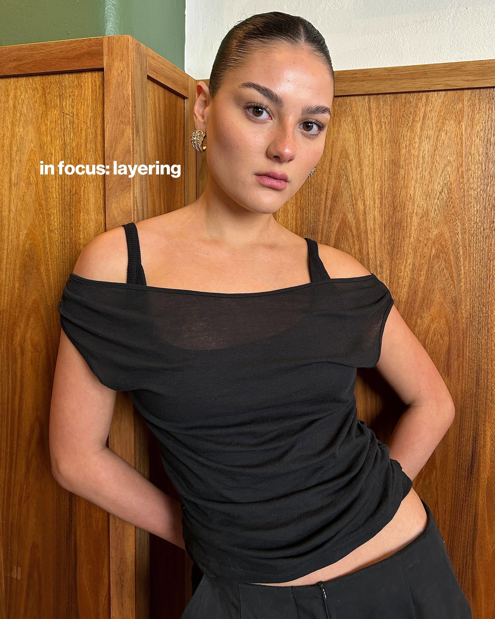 A medium shot shows a person wearing a black off-the-shoulder top and black pants, standing in front of a wooden cabinet, with the text 'in focus: lay...