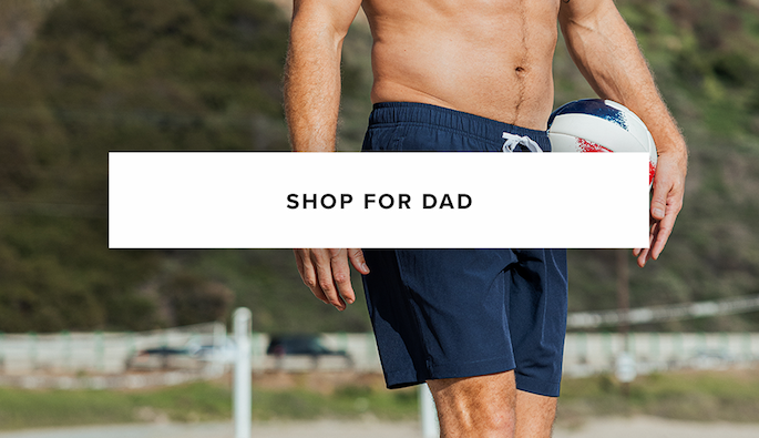 Close-up of a shirtless man on a beach holding a volleyball, wearing navy blue swim trunks. Text reads: "Shop For Dad."