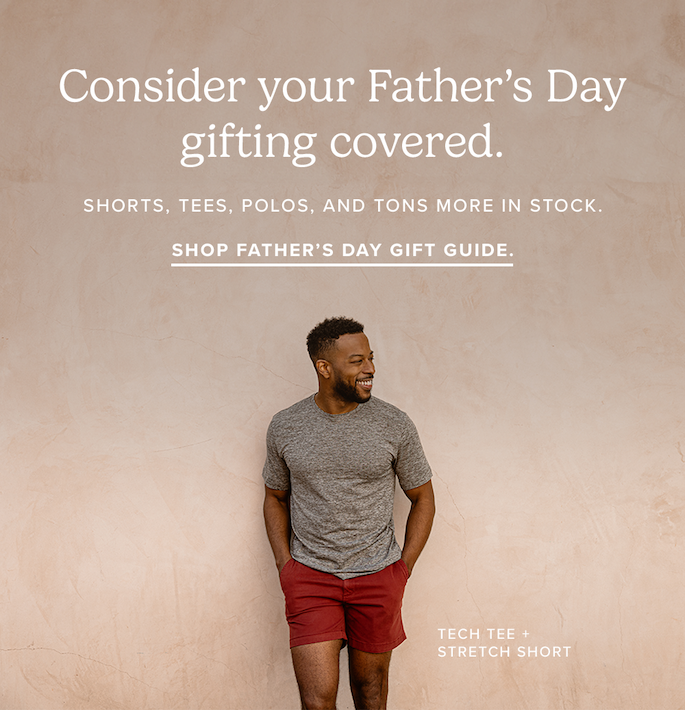A man in a grey t-shirt and reddish-brown shorts stands smiling against a textured beige wall. Text reads: "Consider your Father's Day gifting covered. Shorts, tees, polos, and tons more in stock. Shop Father's Day Gift Guide. Tech Tee + Stretch Short."
