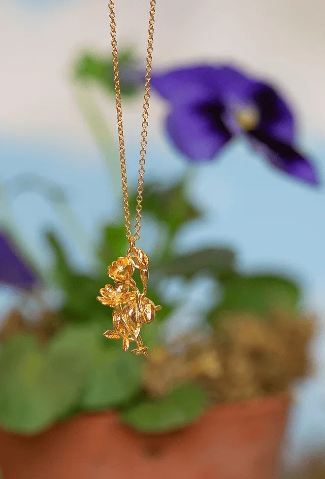 Gold floral pendant necklace with purple flowers in the background.