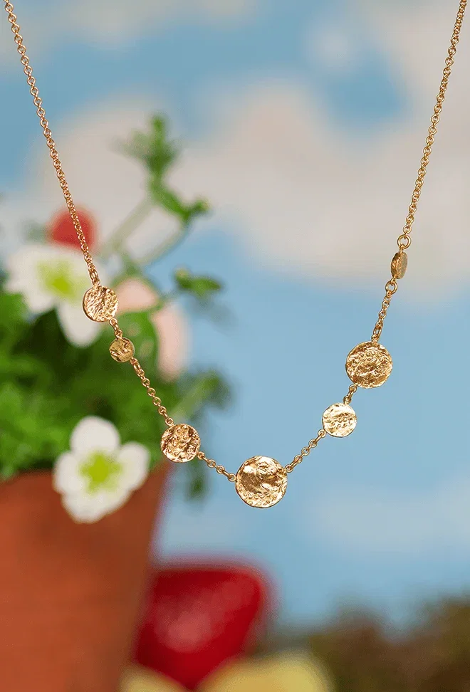 Gold textured disc necklace against a soft floral background.