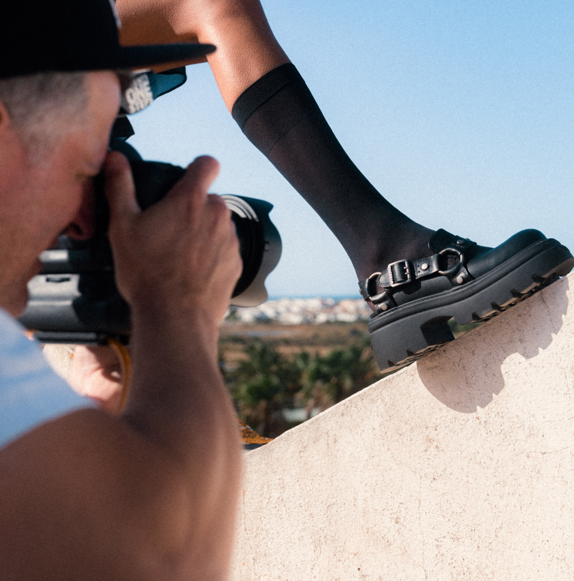 Close-up of a black platform sandal with buckle detail on a raised foot, photographed outdoors during a photoshoot.