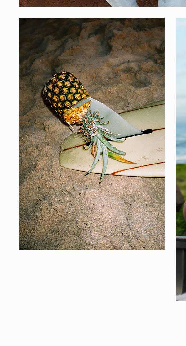 Surfboards laid out on the beach at sunset with a pineapple on the fin