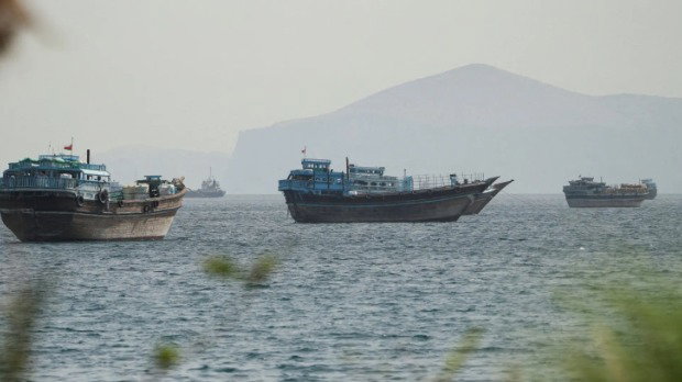 A handful of boats are sailing on a body of water in front of a misty sky and hills.