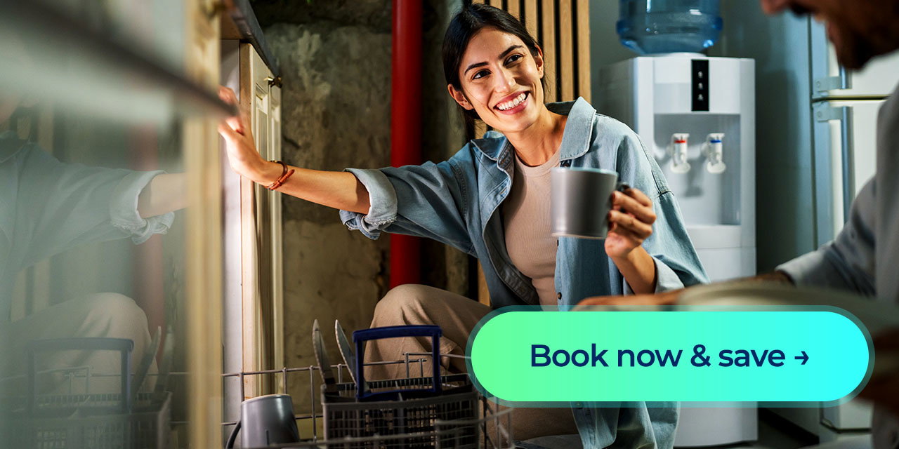 A woman smiling while loading cups into a dishwasher in her kitchen, with a 'Book now & save' button displayed in front