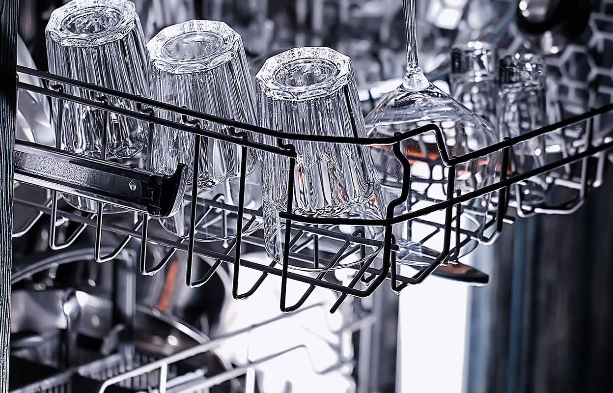 Clean glasses and stemware arranged upside down in a dishwasher rack after a wash cycle