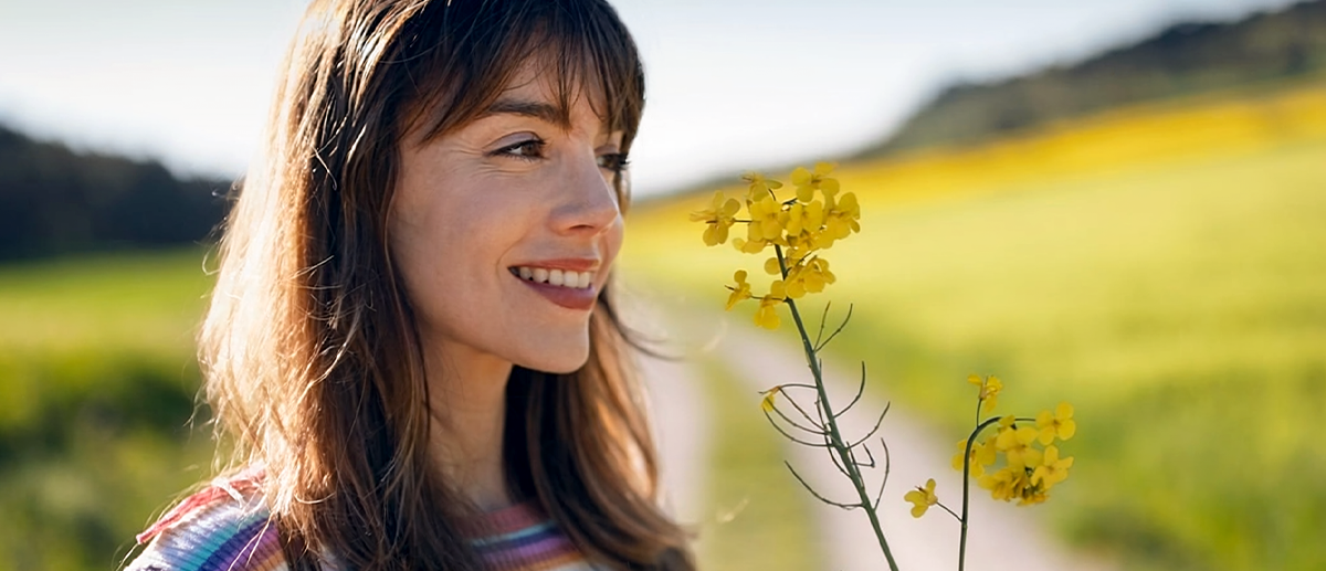 Lächelnde Frau hält gelbe Blumen auf einer blühenden Wiese und genießt die Frühlingssonne.