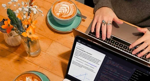 A table with cups of coffee, flower vase, and laptops