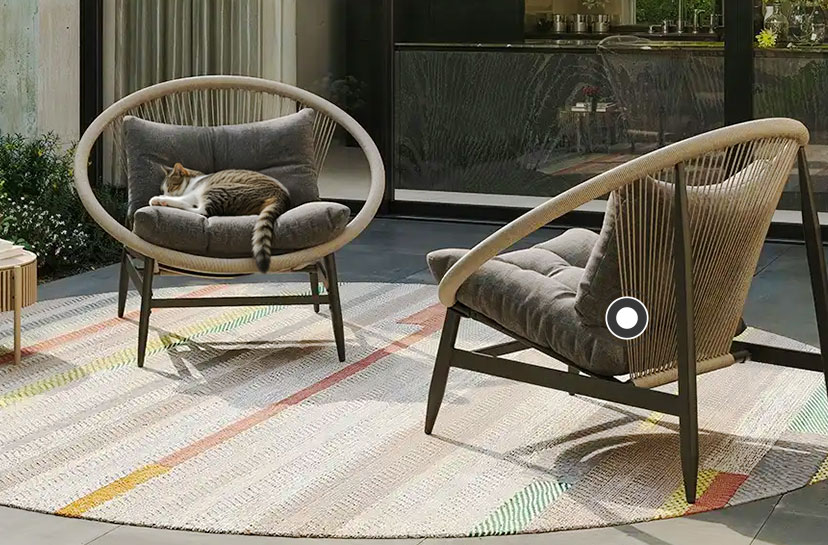 Zwei moderne, korbähnliche Sessel mit runden, oval geschwungenen Rahmen und dunkelgrauen Polstern stehen auf einem großen, runden Outdoor-Teppich mit dezenten, farbigen Streifen. Auf dem linken Sessel liegt eine schlafende Katze. Über der Szene steht der Text "Lounge Möbel"