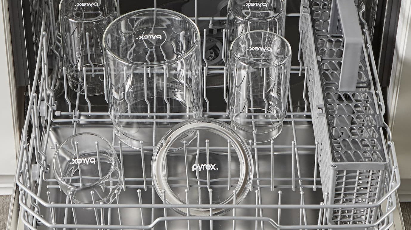 Pyrex glass canisters placed inside a dishwasher rack for cleaning.