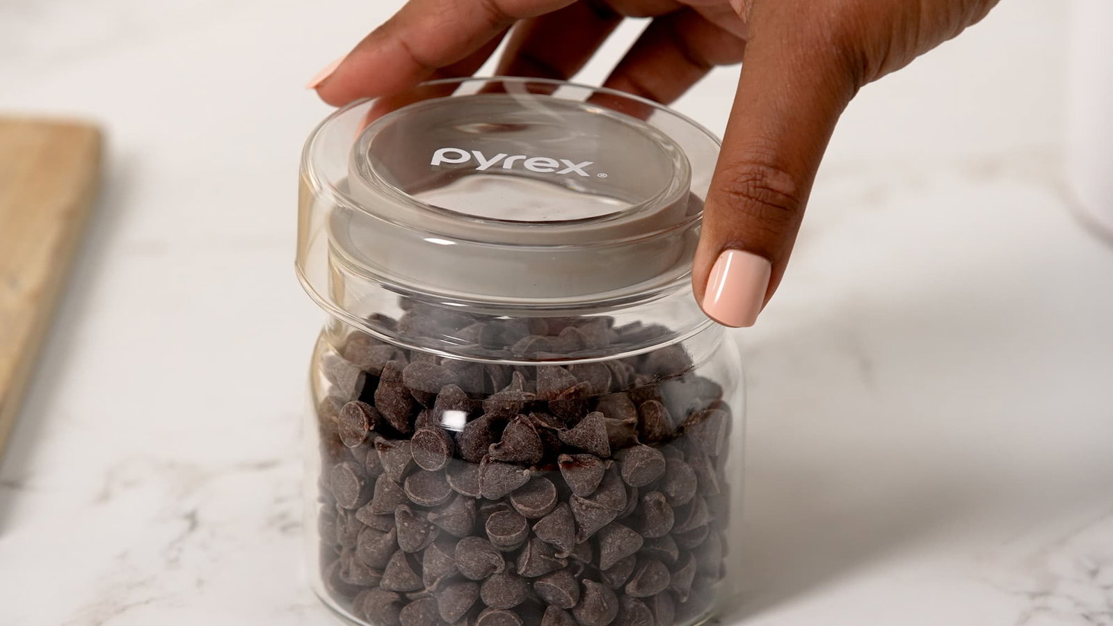Hand opening a Pyrex glass canister filled with chocolate chips.