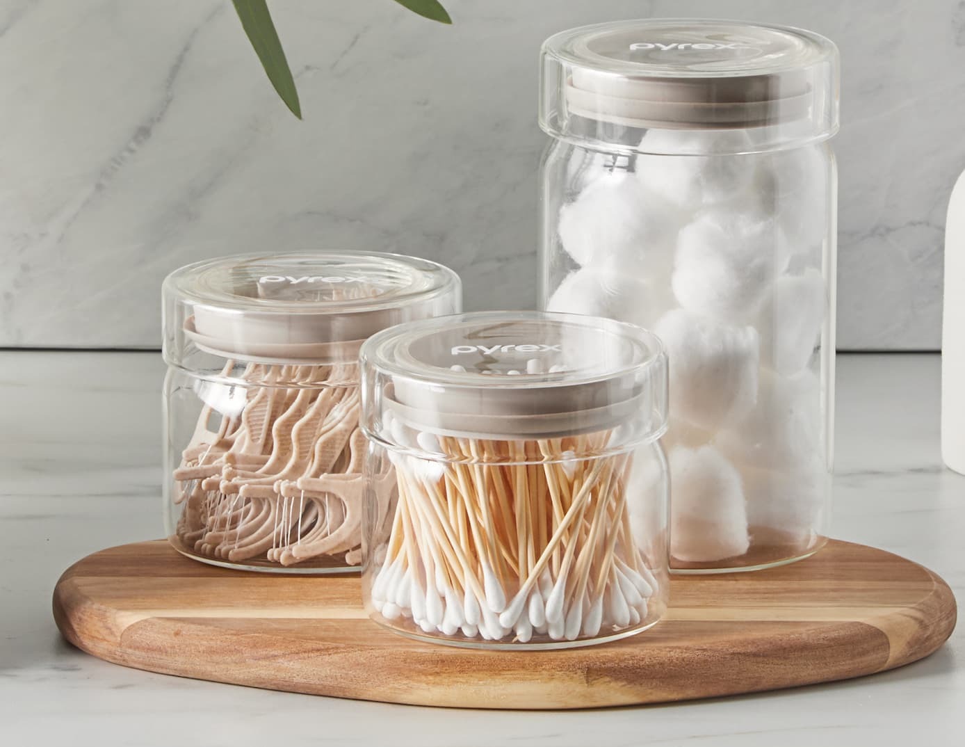 Glass canisters storing cotton balls, swabs, and household essentials on a tray.nister.