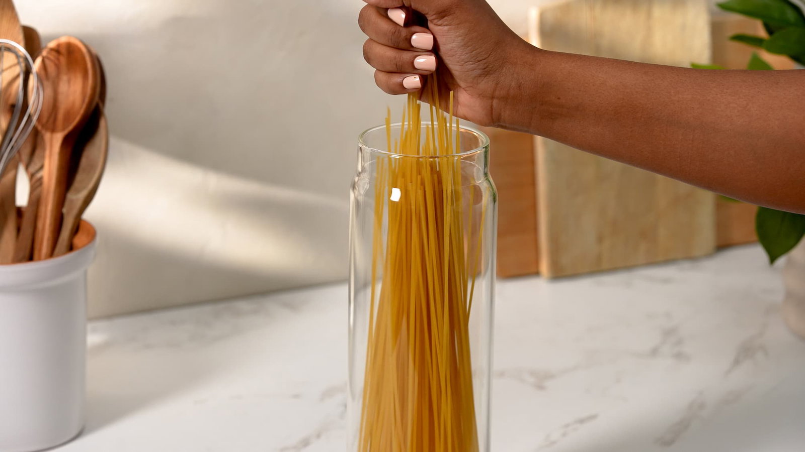 Hand placing spaghetti into a tall glass canister.