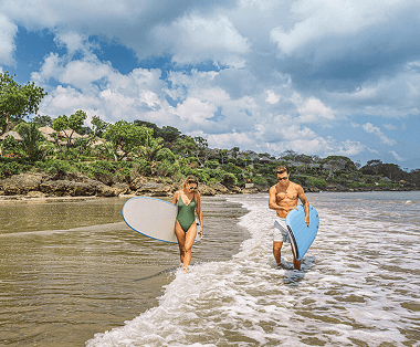 Two surfers walk along the beach, carrying surfboards.