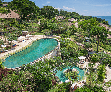 Lush resort with a large pool overlooking the ocean and greenery.